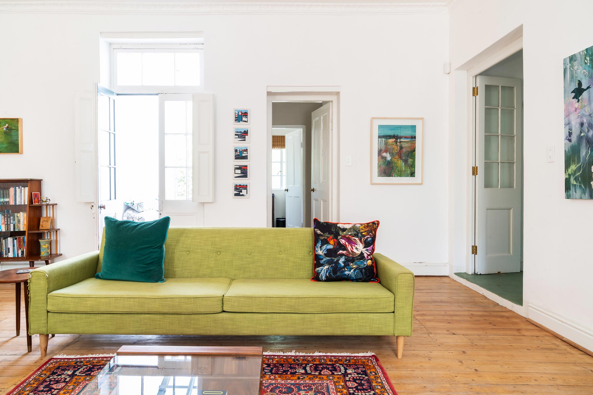 Green couch with a black floral pillow and colourful art