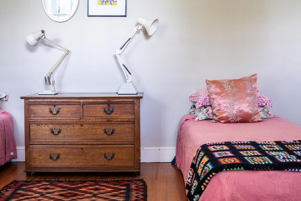 Pink bedroom with antique dresser and bold patterns and colours